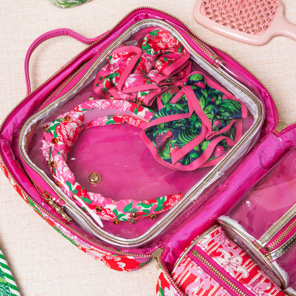 A twisted fabric headband featuring a vibrant pink floral print with green leaves, decorated with gold-tone beads and dark red jewel embellishments in a travel case